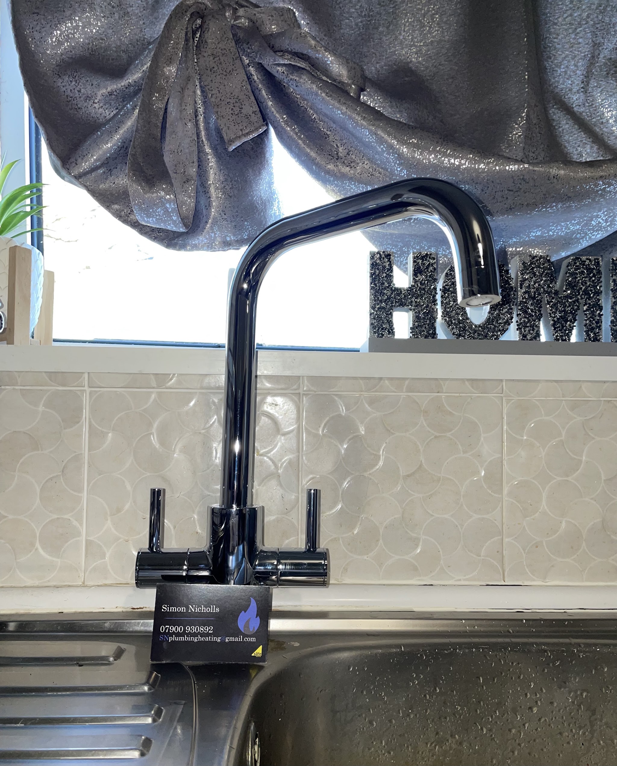 New black mixer tap on a kitchen sink, with Simon's business card on the drainer